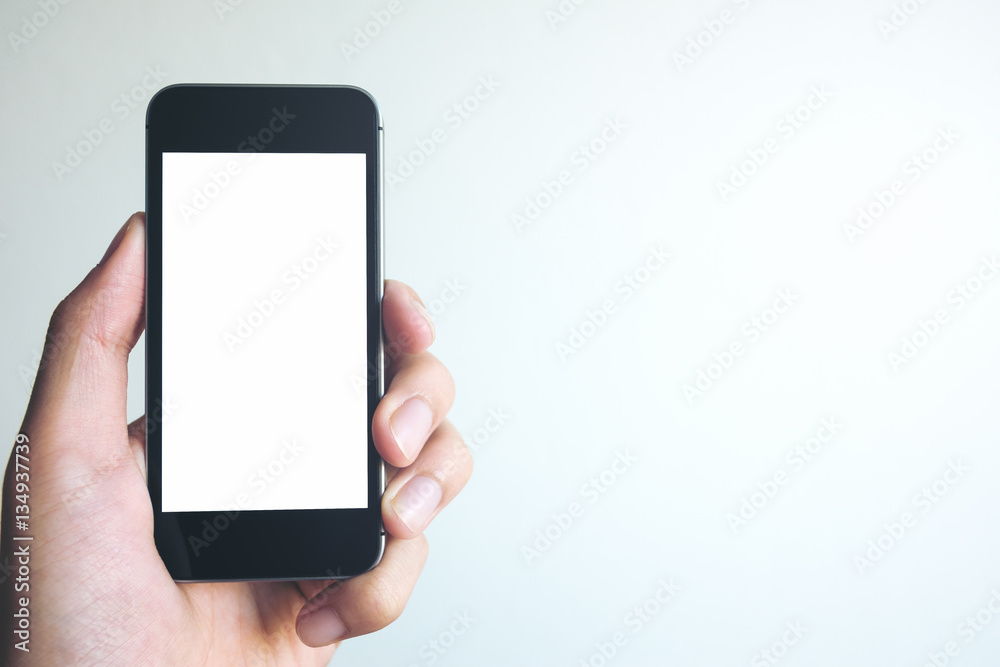 Mockup image of hand holding black mobile phone with blank white screen on white background room Mockup image of hand holding black mobile phone with blank white screen on white background room