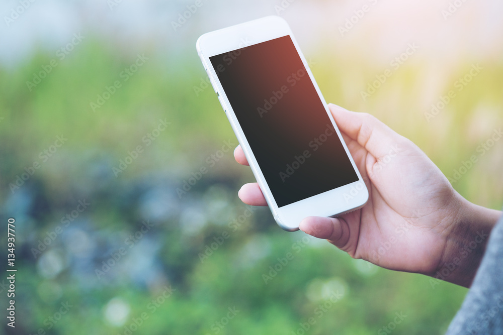 Mockup image of using smart phone with blank black screen at outdoor and nature background