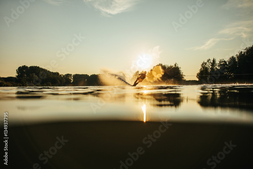 Wakeboarder skiing on lake at sunset
