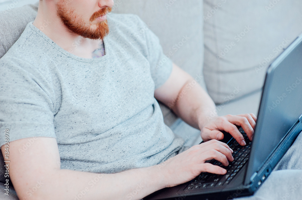 Naklejka premium stylish man with a laptop on the sofa at home