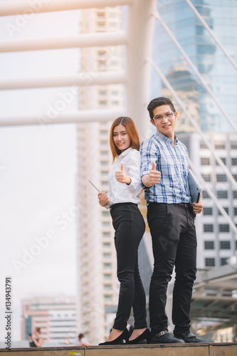 Young Businessman and businesswoman holding digital tablet and computer laptop with colleagues in background at walkway at city.technology and teamwork concept