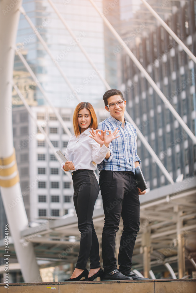 Young Businessman and businesswoman holding digital tablet and computer laptop with colleagues in background at walkway at city.technology and teamwork concept