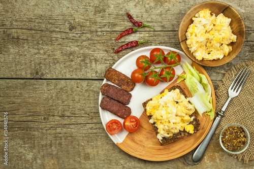 Scrambled eggs with bread and salami. Egg breakfast on a wooden table. Healthy food.