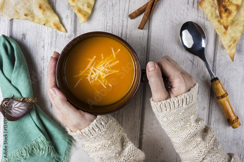 Hands holding bowl with homemade soup on wooden table, top view 