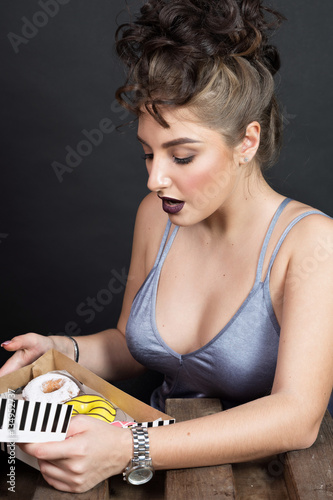 Slim beautiful woman eating a doughnut. Fashionable young woman looking in a box with doughnuts