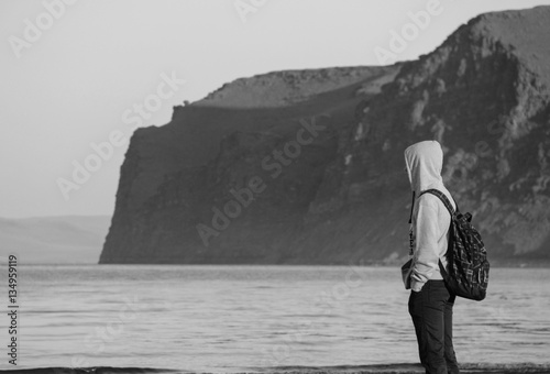 Человек в капюшоне у моря на фоне скал