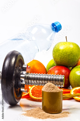 Concept of healthy active lifestyle. Green and red apples and red orange slices. Bottle with pure drinking water. Scoop with whey chocolate protein in foreground. Fitness dumbbell. White background.