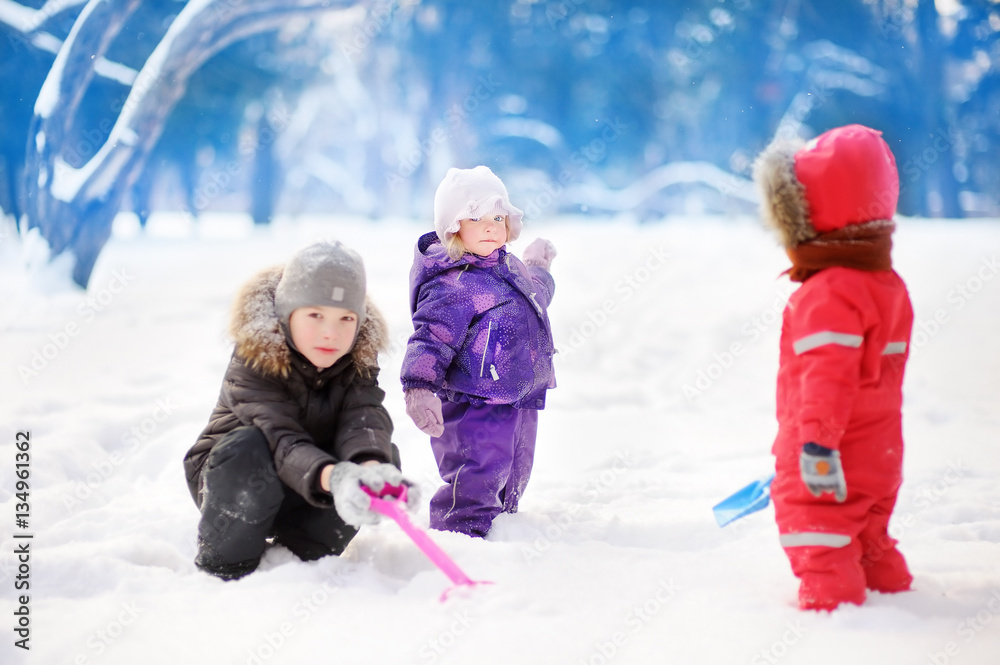 Little children in winter clothes having fun in park at the snowy winter day