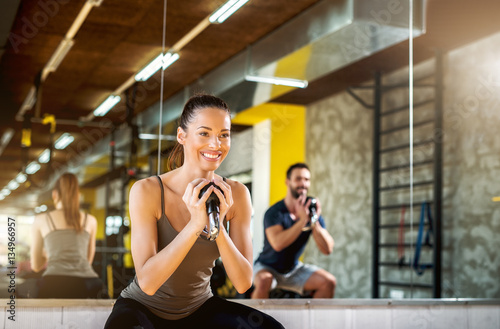 Smiling female working out squats with dumbbells with instructor at the gym.