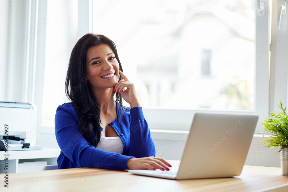 Happy woman sitting at her desk working with notebook Happy woman sitting at her desk working with notebook