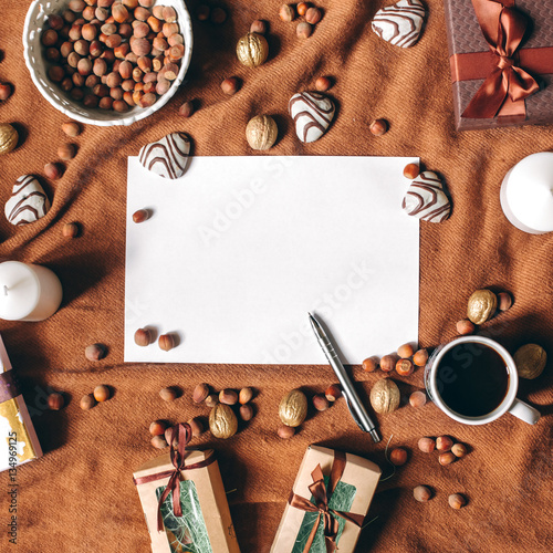 Romantic style background with empty sheet in center, heart shaped biscuit, pen, coffee cup, gifts, nuts on brown fabric cover. Copyspace, top view, flat lay