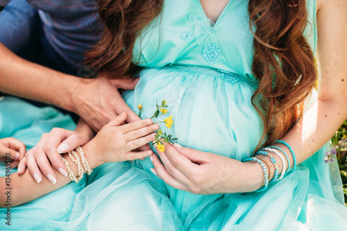 Parents hands holding flower on the pregnant belly. Family concept.