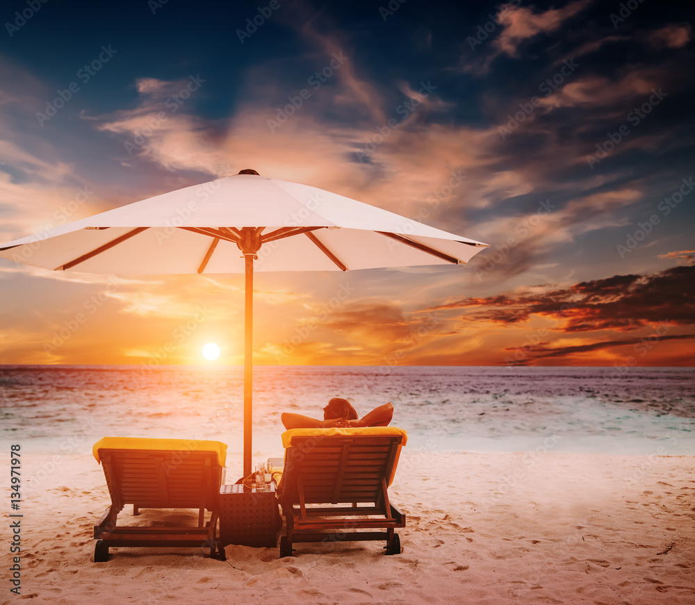 Woman on sunbed under umbrella at sunset
