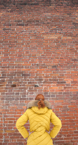 The girl in the yellow jacket looking at a brick wall