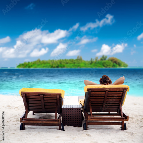 Woman on sunbed at tropical beach near green island