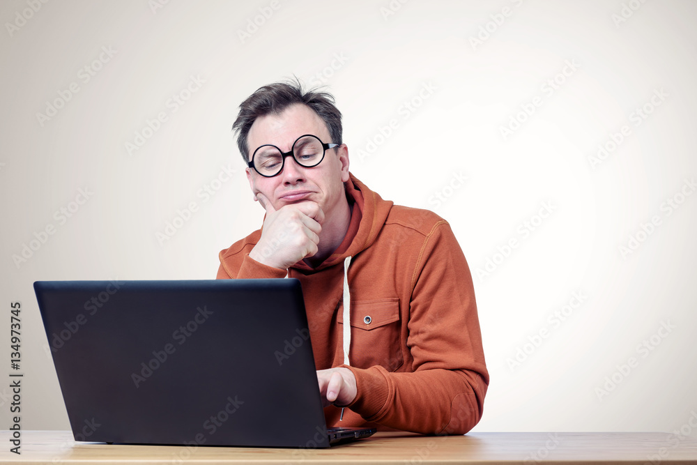 Programmer with glasses and a sweatshirt thinking in front of laptop Programmer with glasses and a sweatshirt thinking in front of laptop
