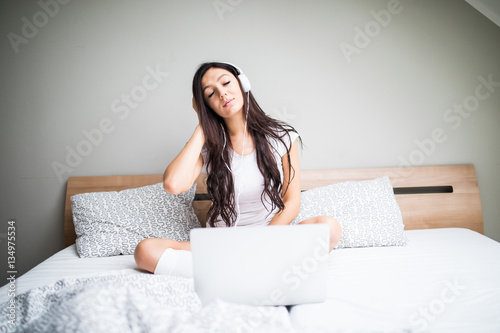 Beautiful young woman listening to music in headphones from laptop at home