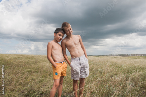 young boys standing in a field. boys in shorts. Boys stand in the desert. feather in the field. boy looking up at the sky. dreamer. two brothers. two friends. children playing in the field.