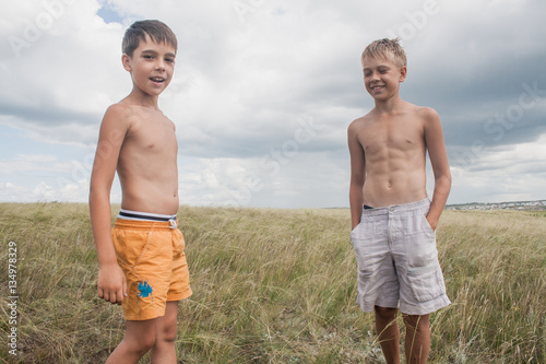 young boys standing in a field. boys in shorts. Boys stand in the desert. feather in the field. boy looking up at the sky. dreamer. two brothers. two friends. children playing in the field.