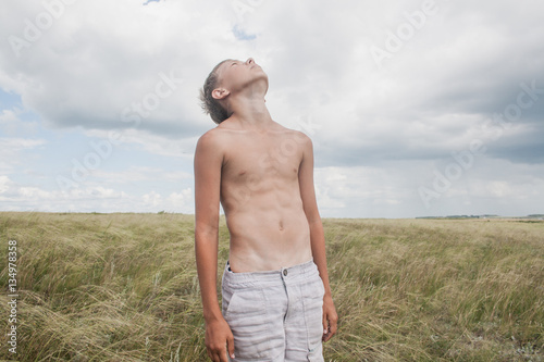 young boy stands in a field. boy in shorts. boy stands in the desert. feather in the field. boy looking up at the sky. dreamer