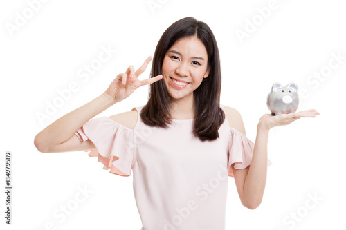 Asian business woman show victory sign with pig coin bank.