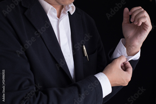 A business man in black suit is dressing up, fastening closing shirt sleeve buttons.