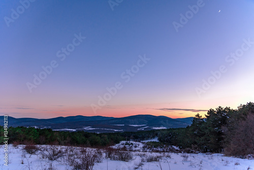 Gorgeous red sunset with mountain views and a crescent moon with a polar star in the corner. Russia, Stary Krym.