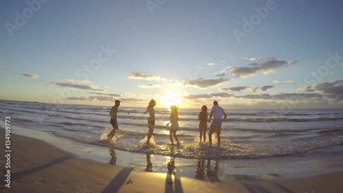 Group of friends running towards the sea on a beautiful beach at sunrise