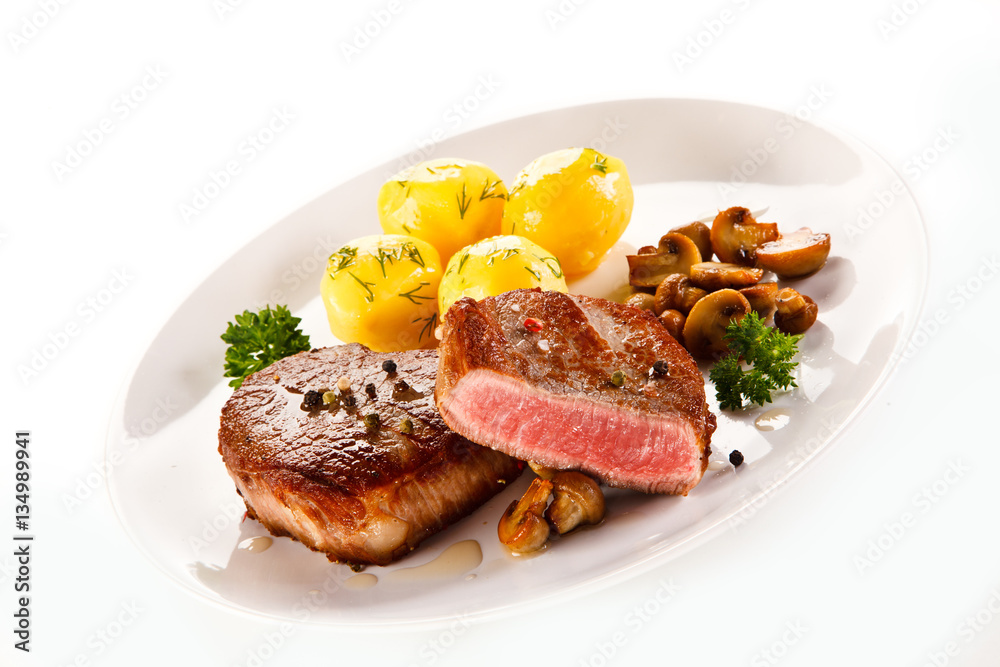 Grilled steaks, boiled potatoes and vegetable salad on white background Grilled steaks, boiled potatoes and vegetable salad on white background