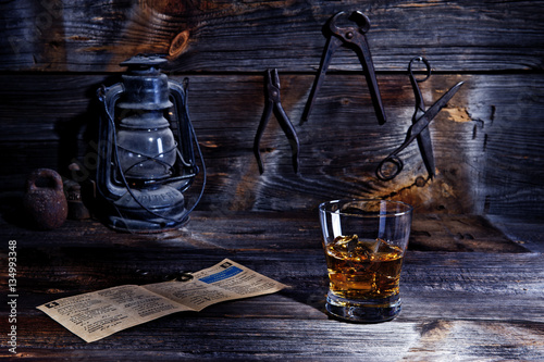 A glass of whiskey on a wooden table in an old workshop