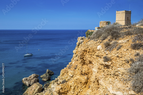 Malta - Sail boat at Ghajn Tuffieha tower on a hot summer day with crystal clear blue sea water