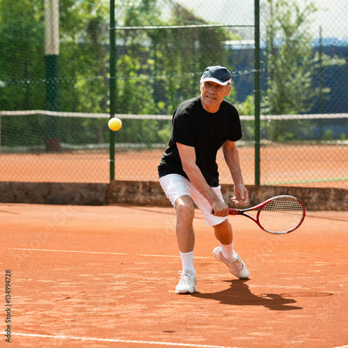 Senior men hitting ball on tennis court © Microgen