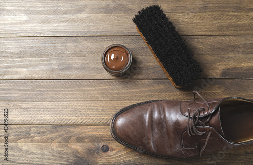 Dirty brown shoe next to brush and cream on wooden table. Horizontal shoot.
