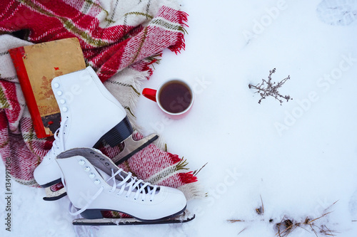 Winter vacation: tea, ice skates with a red blanket in the cage in the snow