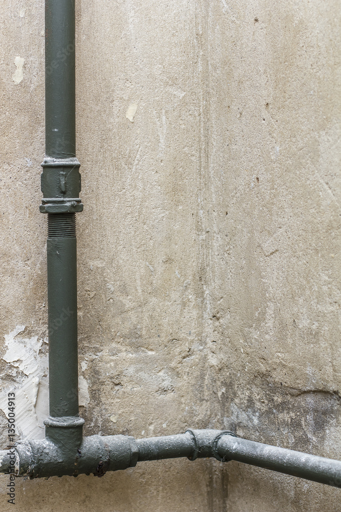 On the wall in a corner an old heating pipes are covered with dust, without a radiator.
