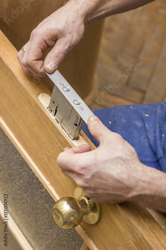 Carpenter establishes the in a wooden door mortise lock. photo