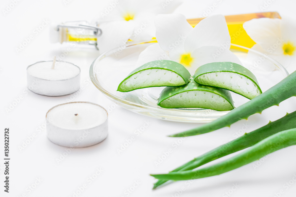 Fresh aloe vera slices with leaf, flowers, candels and oil on wh