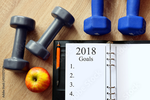 Dumbbells with apple and open notebook on wooen desk. Healthy resolutions for the New Year 2018. photo