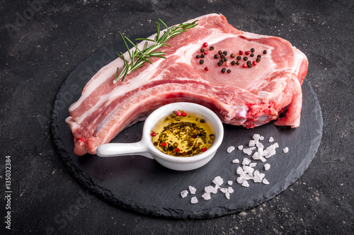 Raw meat on dark background. Raw pork steak with herbs, oil and spices. Cooking meat. Copy space