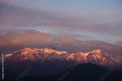 Scenic view of beautiful sunset over the Himalayas with red tint on snowy peaks and white clouds in sky. Amazing landscape of snow capped mountains at sunrise. Beauty, nature and environment