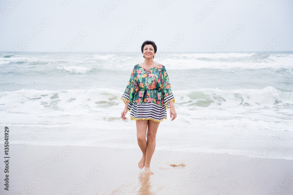 Happy healthy mature woman walking, Enjoying freedom on the Ocean Beach. Travel Vacation. Wellness and Happiness Lifestyle Concept