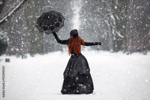 Mysterious red-haired woman in Victorian dress in the winter par