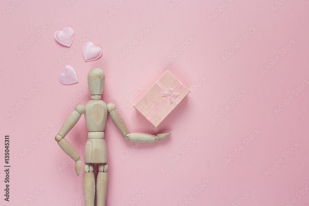 Classic wooden dummy holds gift box and hearts on a pink backgro