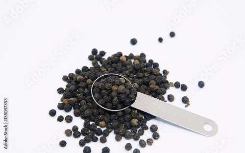 Black peppers in teaspoon isolated on white background