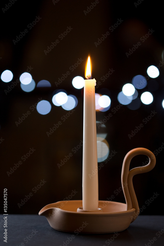 Portacandela con candela bianca accesa su superficie nera e sullo sfondo  luci notturne Stock Photo