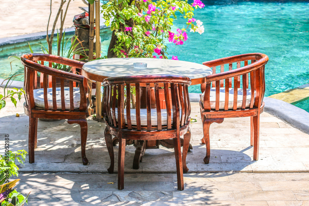 Wooden table and chairs in tropical balinese style near pool