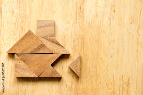 Tangram puzzle in home shape with the missing piece on wooden background