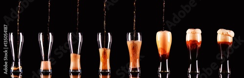 Many glasses with dark beer or kvass with foam pouring on black background on different levels.