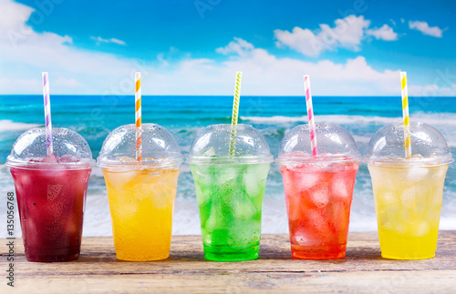 colorful cold drinks in plastic cups on the beach