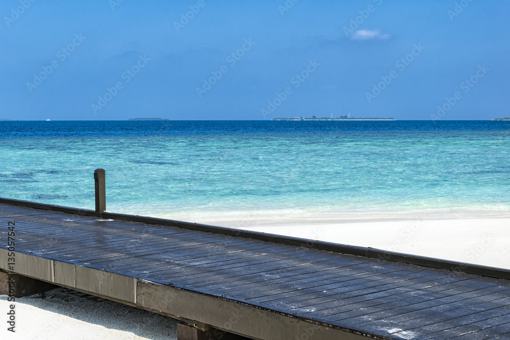 Black wooden pontoon heading in to the indian ocean located on a white sand beach somewhere on maldives.